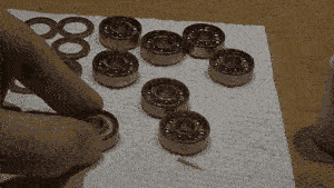 A GIF of bearing shields and exposed bearings scattered around a paper towel with a hand drying one by slamming it against the surface