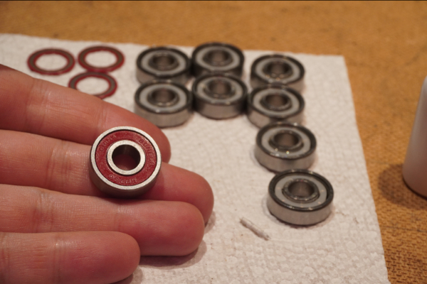 A hand holding a newly cleaned bearing with an out of focus background of bearings on a paper towel with their shields removed.