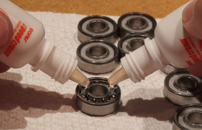 Scattered bearings on a paper towel with 2 bottles of Bones Speed Cream that are applying one drop to a bearing